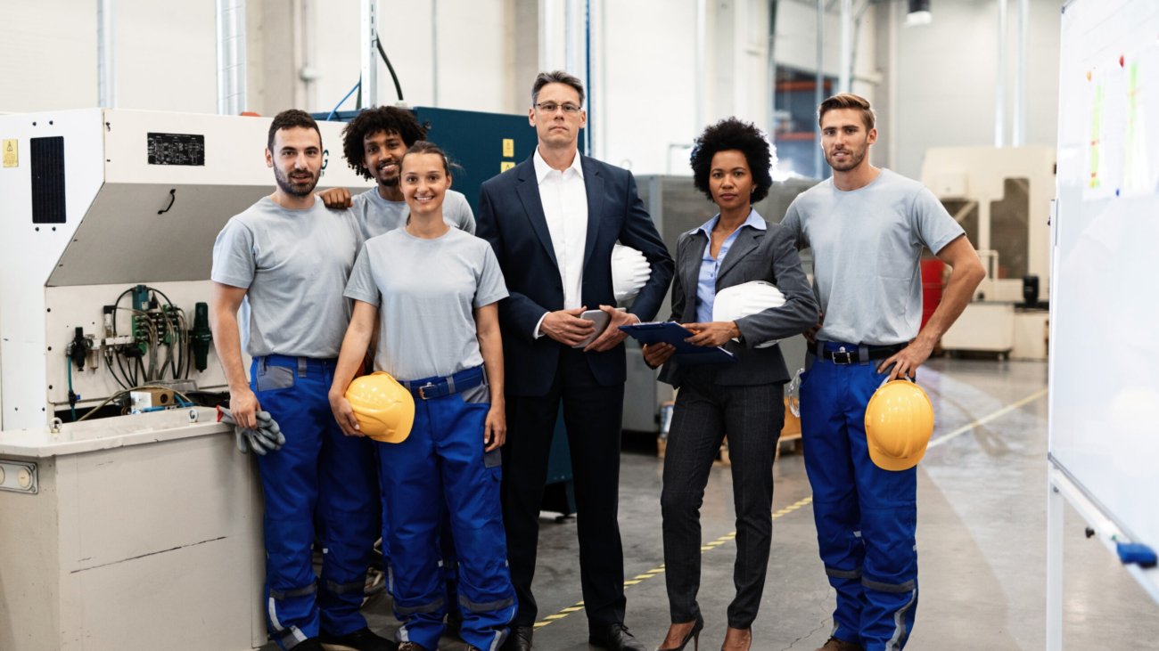 Portrait of group of engineers and corporate managers standing in a factory and looking at camera.
